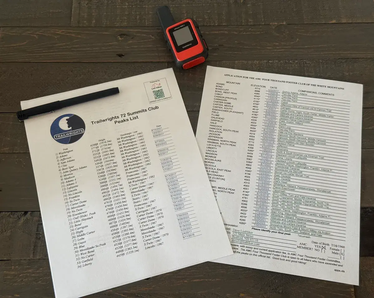 A completed AMC Four Thousand Footer Club application and a Trailwrights 72 Summits Club peaks list, filled in and ready to sign, beside a pen and a GPS device on a wooden table